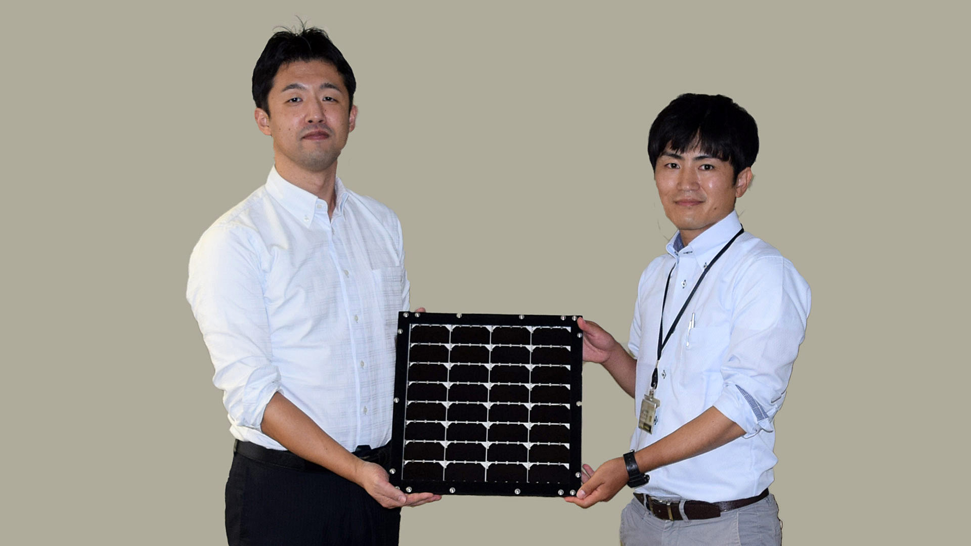化合物事業推進部 主任の植田 浩介（左）と同 田中 康裕 手に持つのは、世界最高水準の「Ⅲ-Ⅴ化合物3接合型太陽電池モジュール」